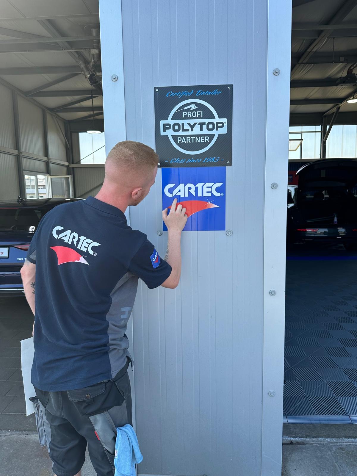 CARTEC-Mitarbeiter befestigt die Plakette „Profi Polytop Partner – Certified Detailer“ neben dem CARTEC-Logo am Werkstatteingang