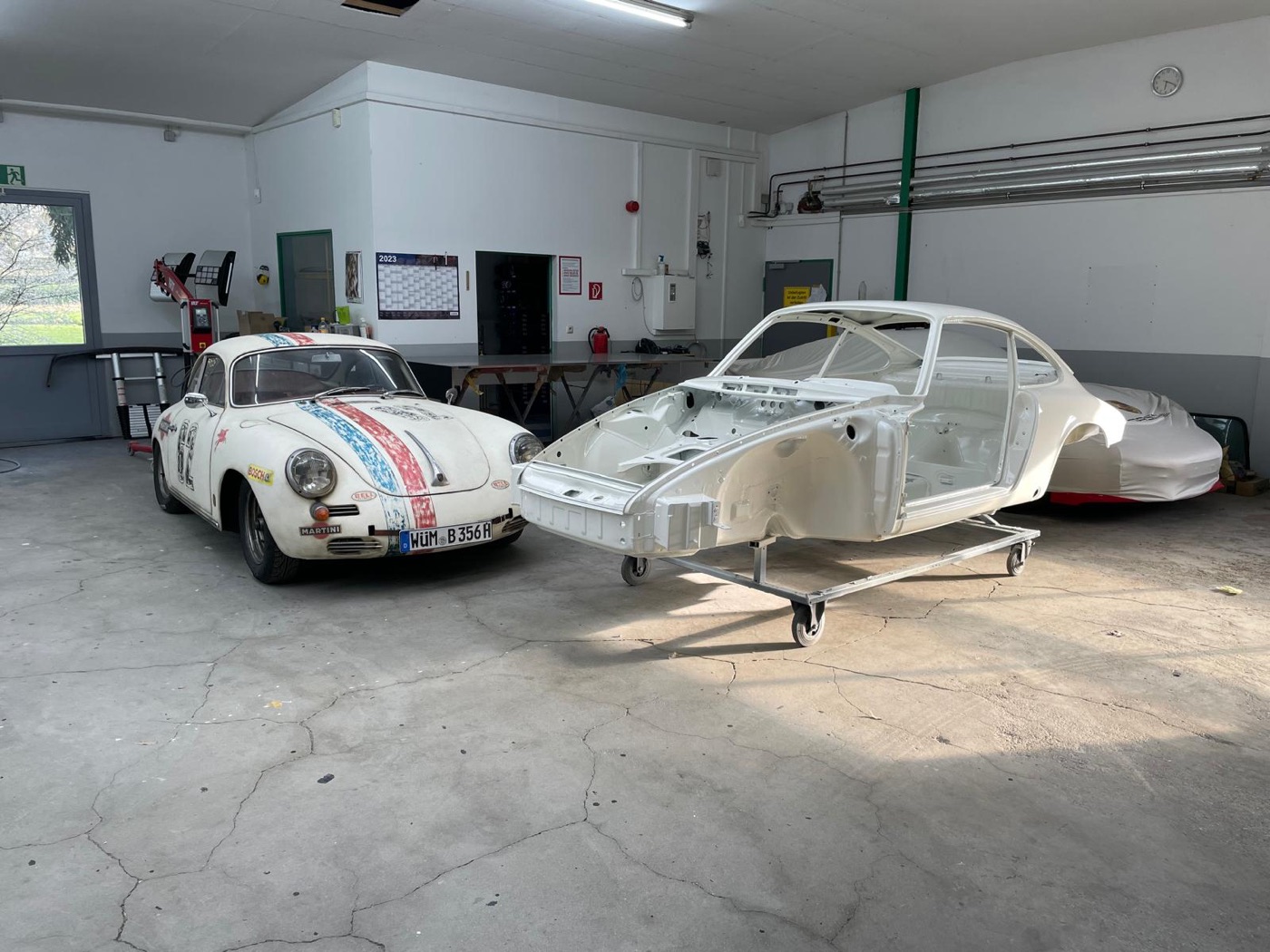 Porsche-Rohkarosserie neben lackiertem Porsche 356 in der Karosserie- und Lackierwerkstatt